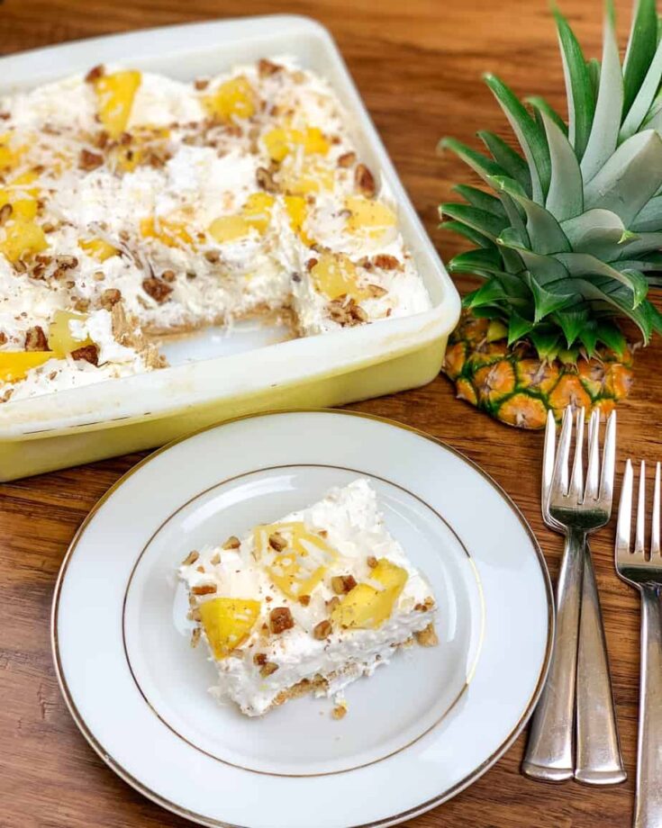 Pineapple lush on a white plate with a casserole dish, pineapple top, and silverware on a counter