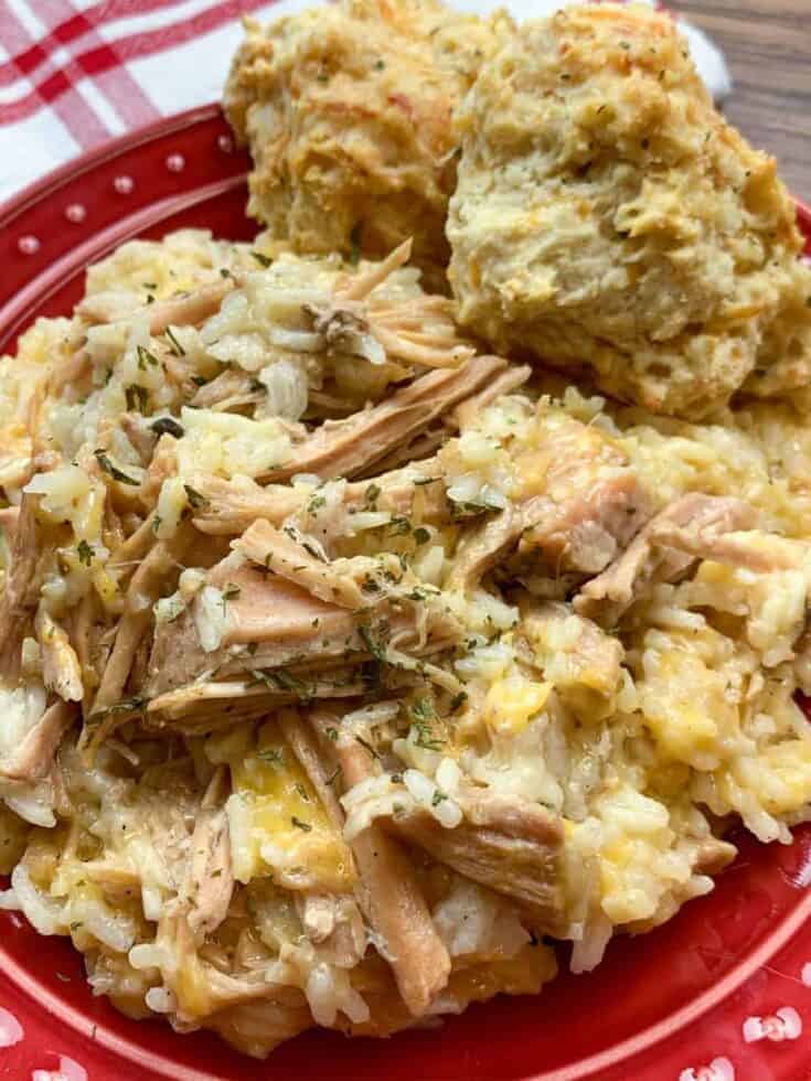 Slow cooker pork chops and rice with cheese on a red plate with two biscuits.