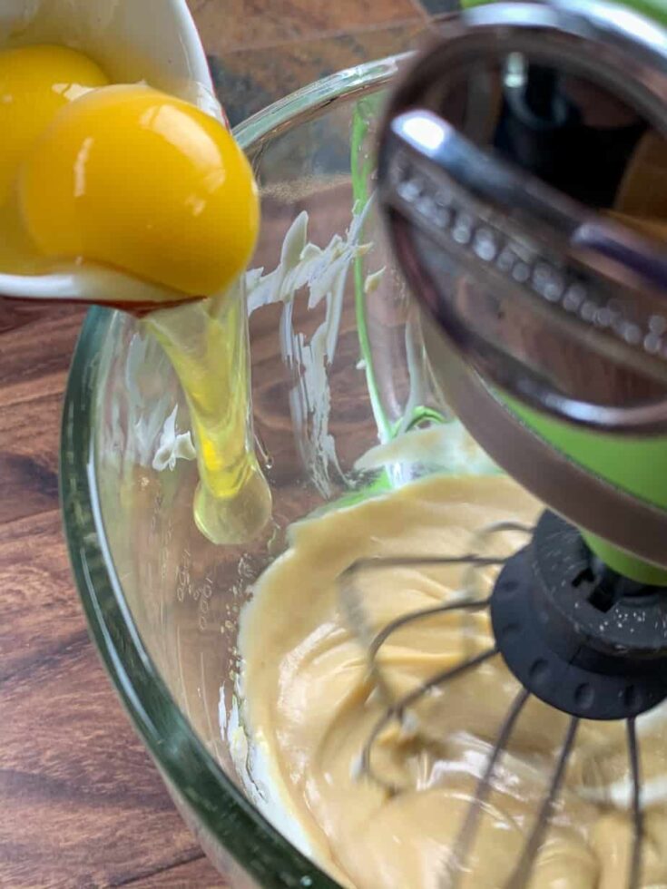 Adding eggs to a donut batter in a large glass bowl