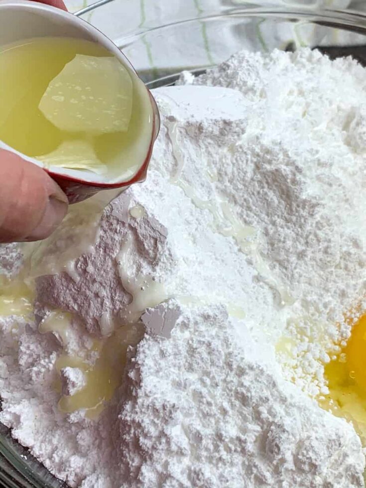 Pouring lemon juice into a bowl with powdered sugar and eggs.