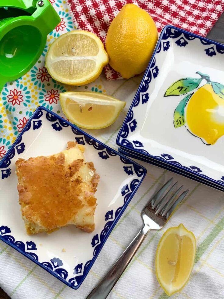 Lemon chess squares on a plate with sliced lemons and a lemon squeezer.