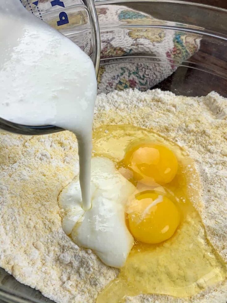 Pouring buttermilk into a glass bowl with cornbread mix and eggs