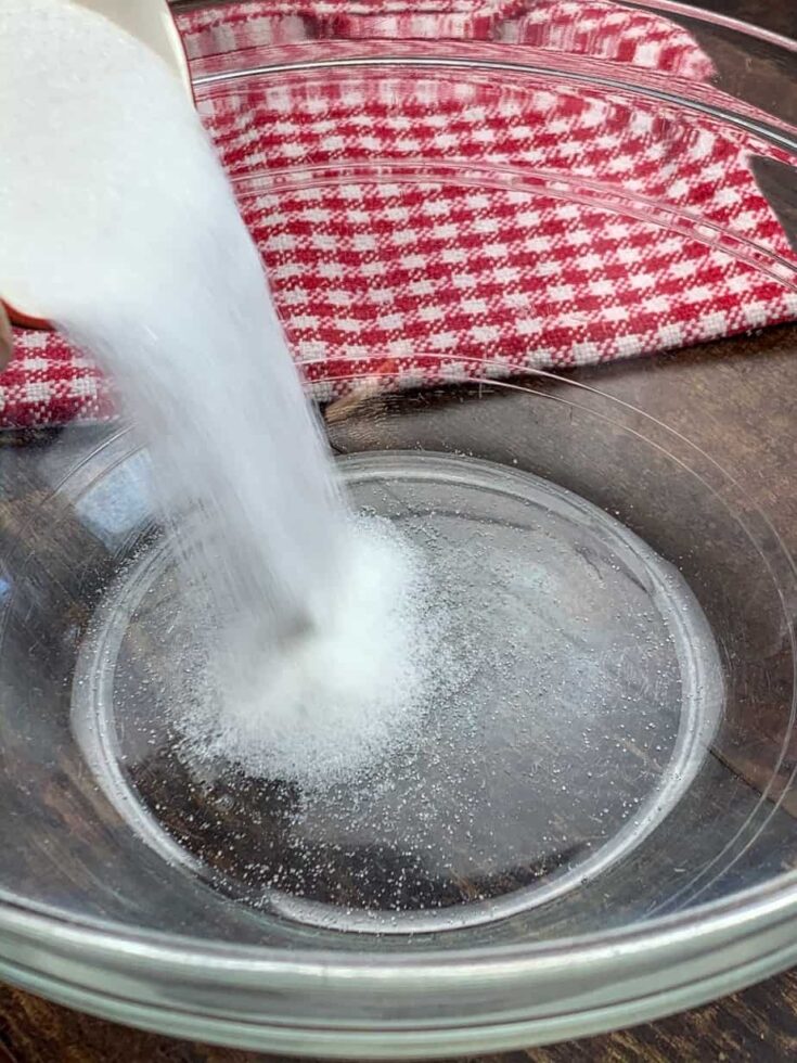 Sugar being poured into a glass bowl for coleslaw