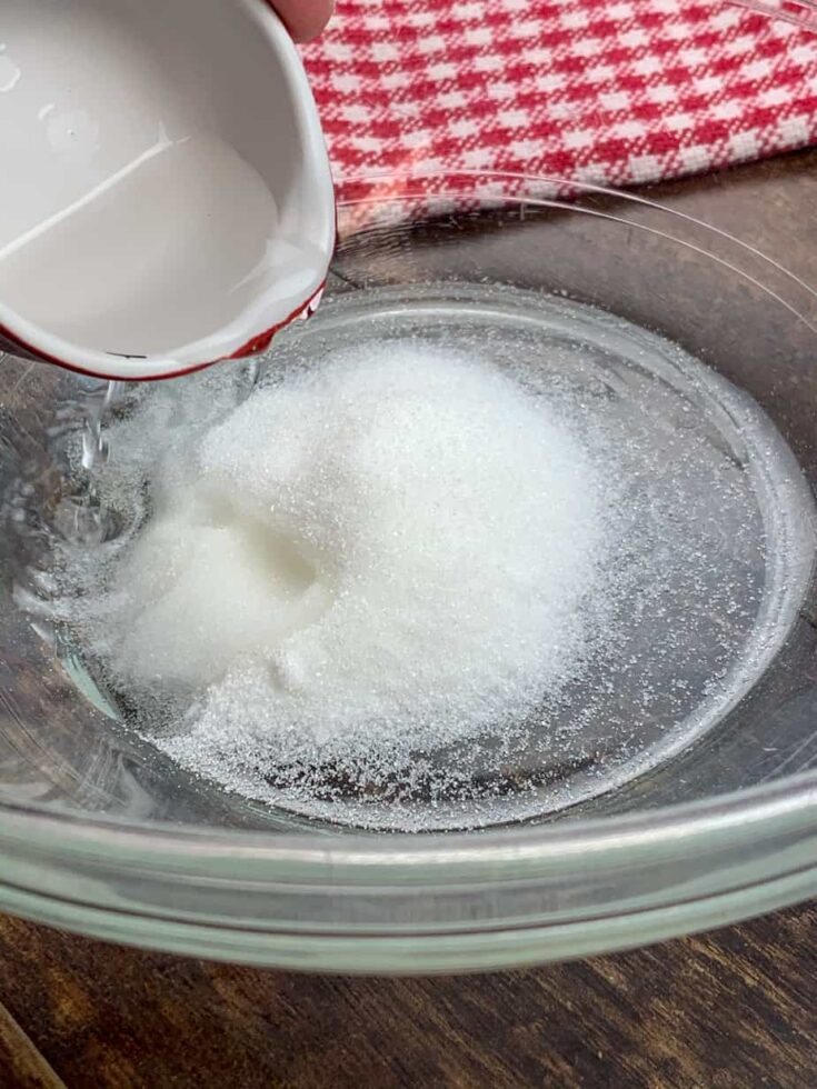 Pouring white vinegar into a glass bowl with sugar