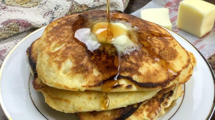 Four cornbread pancakes stacked on top of each other with butter and syrup on top