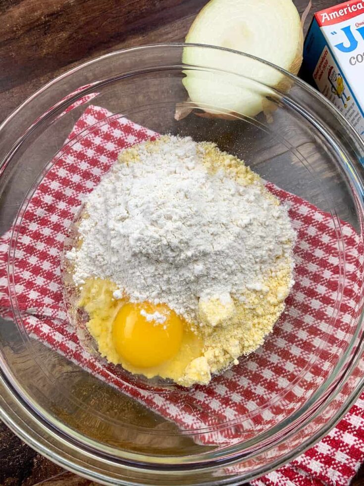 Corn muffin mix, an egg, and flour in a glass bowl. 