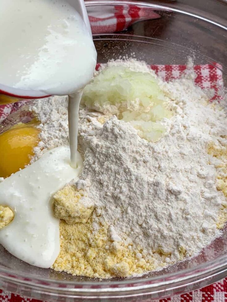 Pouring buttermilk into a glass bowl with hush puppy ingredients. 