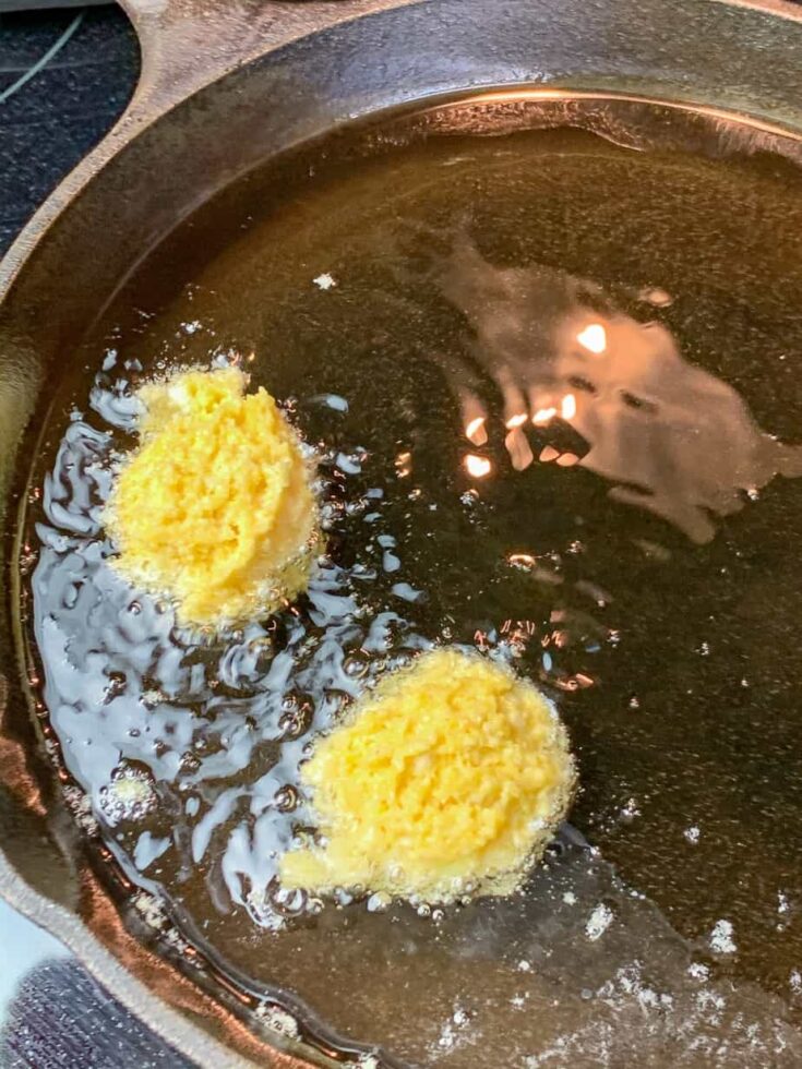 Hush puppies frying in an iron skillet.