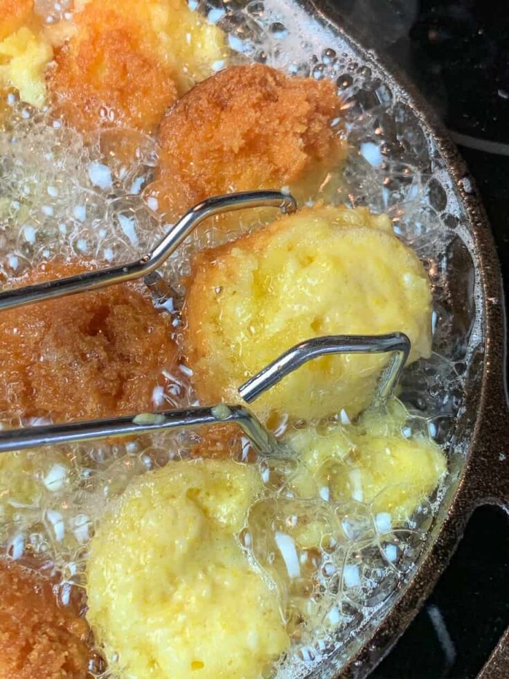 Hush puppies frying in a skillet.