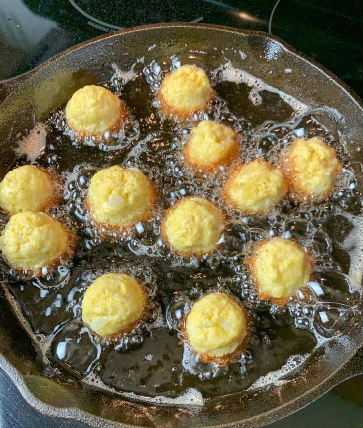 Hush puppies frying in a frying pan.