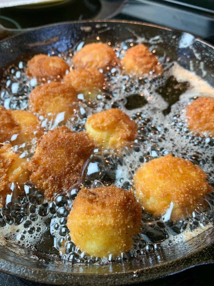 Hush puppies frying in a skillet with oil. 